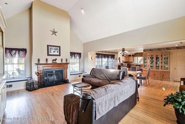 living room featuring a chandelier, light wood-type flooring, and high vaulted ceiling