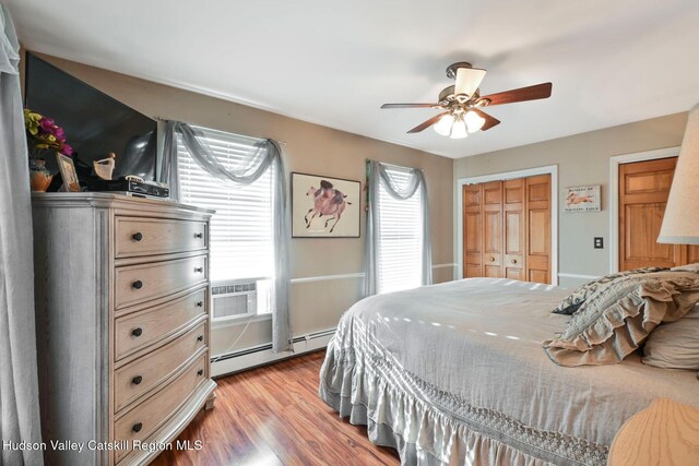 bedroom featuring ceiling fan, baseboard heating, cooling unit, light hardwood / wood-style floors, and a closet