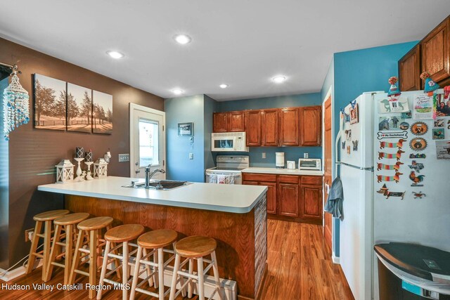 kitchen with light wood-type flooring, white appliances, a breakfast bar area, and sink