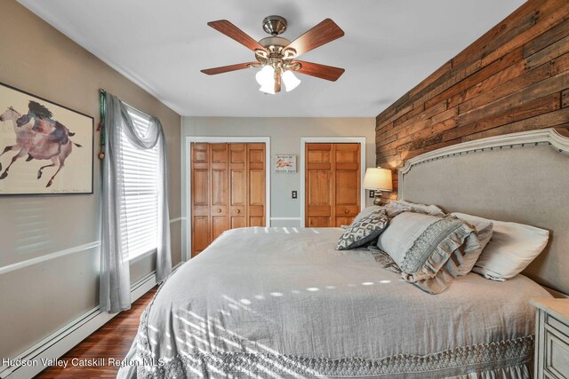 bedroom featuring dark hardwood / wood-style floors, ceiling fan, a baseboard heating unit, and two closets