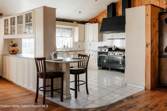 kitchen featuring lofted ceiling, wall chimney exhaust hood, tasteful backsplash, a kitchen breakfast bar, and double oven range