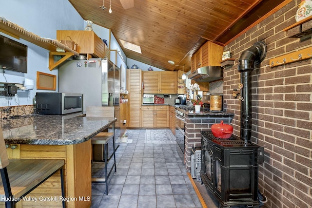 kitchen featuring a wood stove, under cabinet range hood, stainless steel microwave, a sink, and lofted ceiling