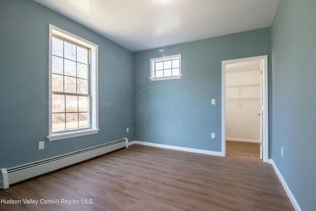 unfurnished room with wood-type flooring, a baseboard radiator, and a healthy amount of sunlight