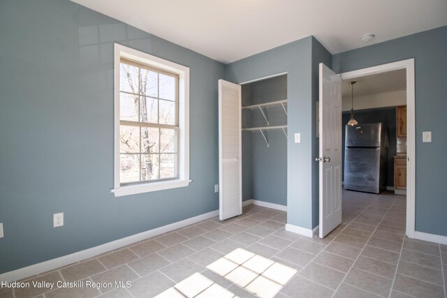 unfurnished bedroom with stainless steel refrigerator, a closet, and light tile patterned flooring