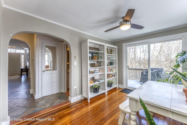 sitting room featuring arched walkways, crown molding, wood-type flooring, ceiling fan, and baseboards