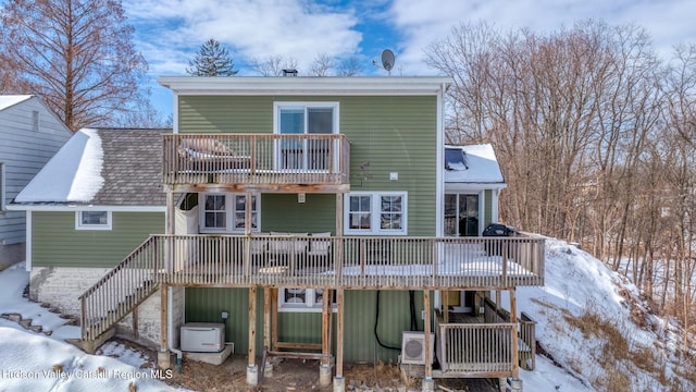 snow covered house with ac unit, a wooden deck, stairway, and roof with shingles