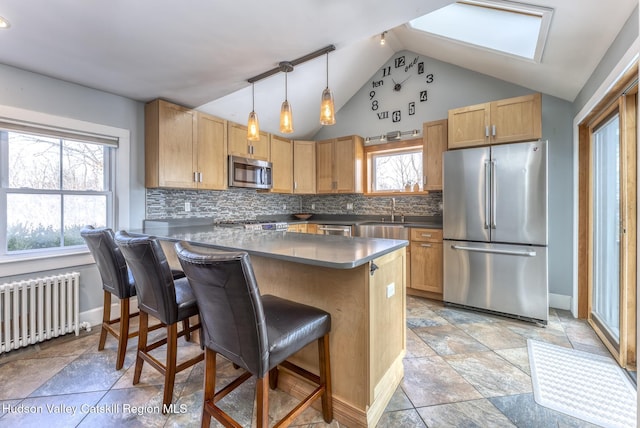 kitchen featuring vaulted ceiling with skylight, a breakfast bar, appliances with stainless steel finishes, decorative backsplash, and radiator heating unit