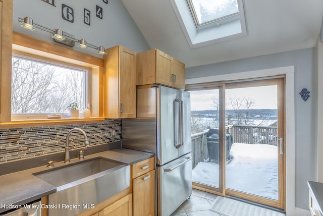 kitchen with a skylight, light tile patterned floors, stainless steel appliances, decorative backsplash, and a sink