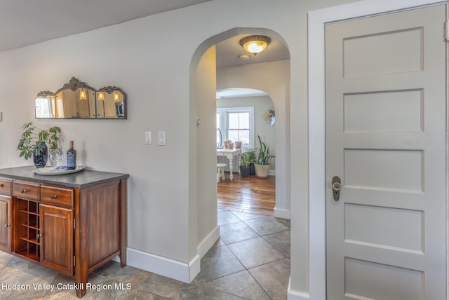 interior space with baseboards, arched walkways, and tile patterned floors