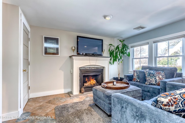 living area with a fireplace with flush hearth, visible vents, baseboards, and stone finish flooring