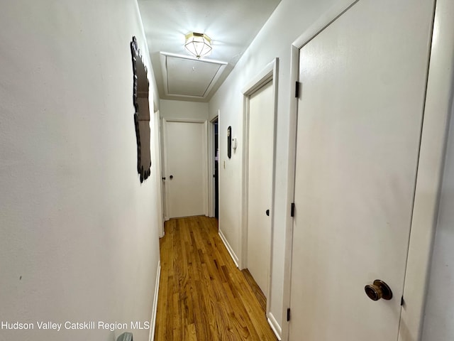 corridor with light wood-style floors and attic access