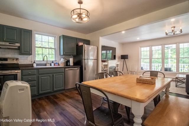 kitchen with sink, dark wood-type flooring, appliances with stainless steel finishes, an inviting chandelier, and tasteful backsplash