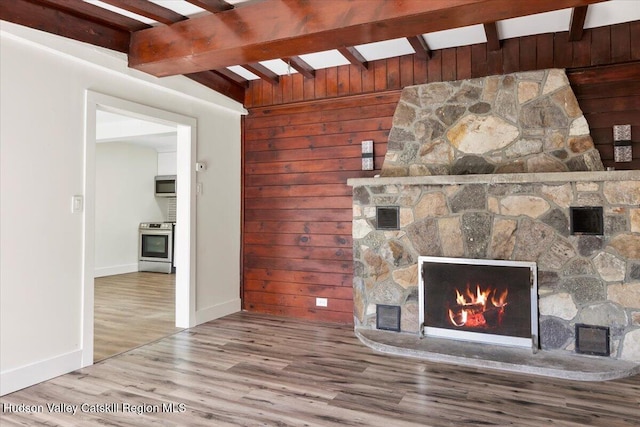 603-607 Old Stage Rd, Saugerties, NY 12477 - unfurnished living room featuring wooden walls, beam ceiling, a stone fireplace, baseboards, and wood finished floors