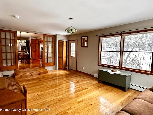 unfurnished living room with light hardwood / wood-style flooring, a baseboard radiator, and an inviting chandelier