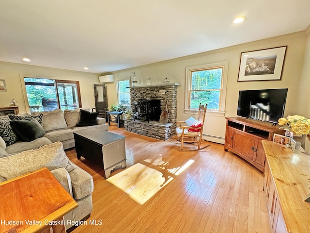 living room featuring light hardwood / wood-style flooring, a wall mounted AC, a baseboard heating unit, and a stone fireplace