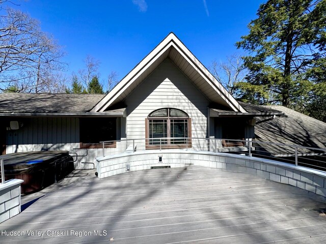 rear view of house featuring roof with shingles, a hot tub, and a deck