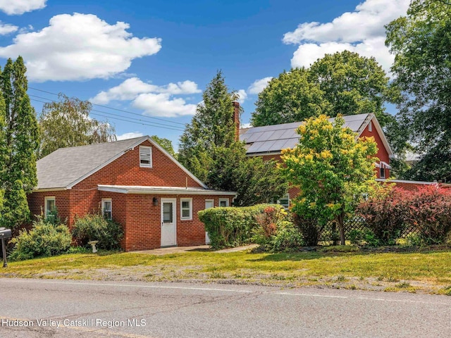2481 Rte 145, East Durham, NY 12423 - view of front of house with brick siding, roof mounted solar panels, a front lawn, and a chimney