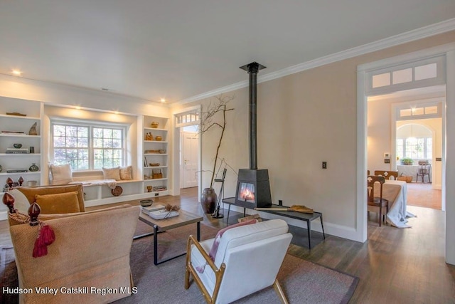 living room featuring built in shelves, wood-type flooring, a wood stove, and ornamental molding