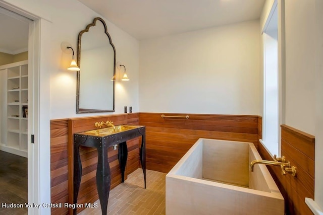bathroom with wooden walls, a wainscoted wall, and a washtub
