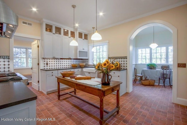 kitchen featuring decorative light fixtures, white cabinetry, tasteful backsplash, and range hood