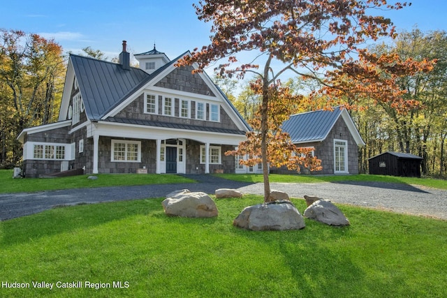 shingle-style home featuring a front lawn, covered porch, metal roof, an outbuilding, and a standing seam roof