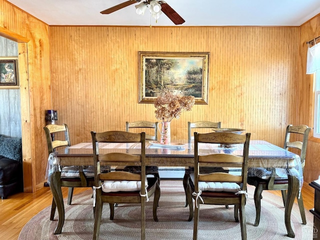 dining area featuring light wood finished floors, ceiling fan, wood walls, a baseboard heating unit, and plenty of natural light