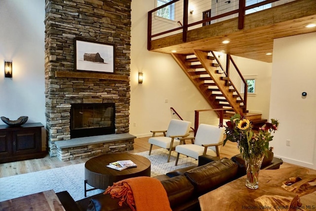 living area with baseboards, a stone fireplace, wood finished floors, and stairway