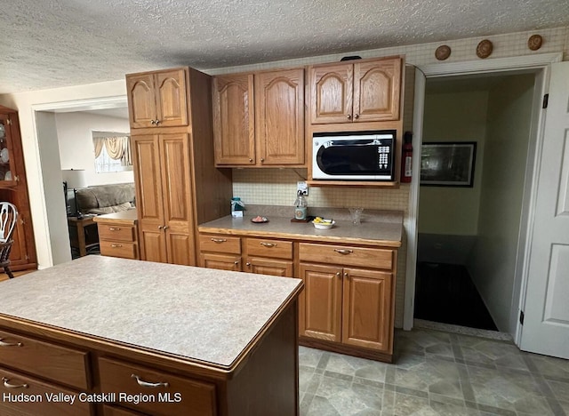51 Patroon St, Claverack-Red Mills, NY 12513 - kitchen with a textured ceiling, light countertops, a center island, decorative backsplash, and brown cabinets