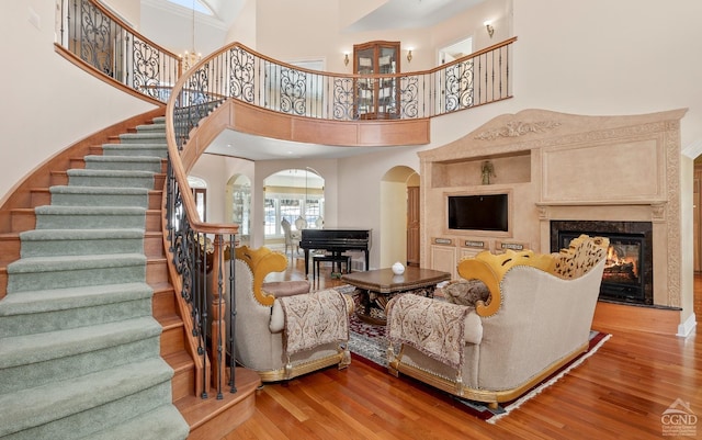 living room featuring stairway, a high ceiling, wood finished floors, arched walkways, and a high end fireplace