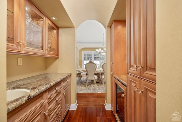 corridor with wine cooler, dark wood-style flooring, a chandelier, baseboards, and a sink
