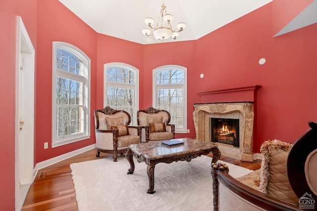 living area with wood finished floors, a chandelier, a premium fireplace, high vaulted ceiling, and baseboards