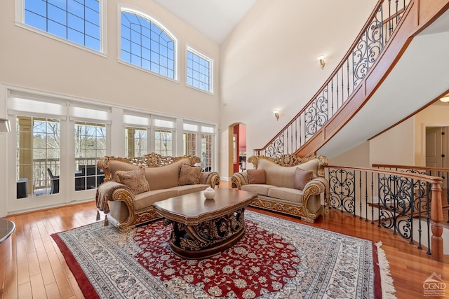 living area featuring a high ceiling, arched walkways, hardwood / wood-style flooring, and stairway