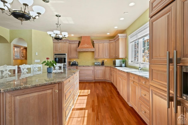 kitchen with custom exhaust hood, arched walkways, a chandelier, light wood-style flooring, and a sink