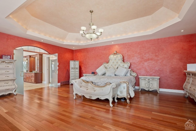 bedroom with a tray ceiling, a chandelier, hardwood / wood-style flooring, and baseboards