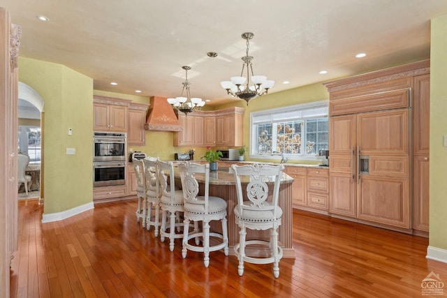 kitchen with appliances with stainless steel finishes, custom range hood, light wood-style floors, a chandelier, and healthy amount of natural light