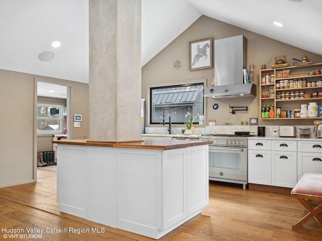 kitchen featuring light countertops, white cabinets, a sink, wall chimney range hood, and high end stove