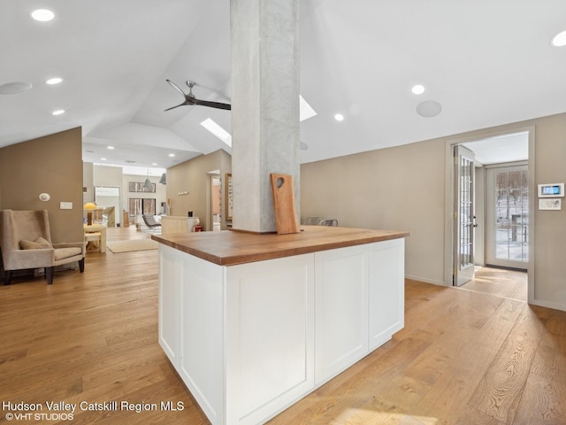 kitchen with wooden counters, lofted ceiling with skylight, open floor plan, white cabinetry, and light wood-type flooring