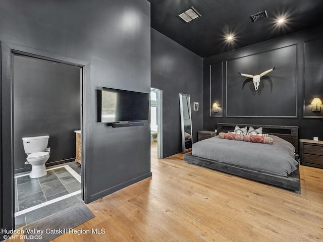 bedroom with a towering ceiling, light wood finished floors, baseboards, and visible vents