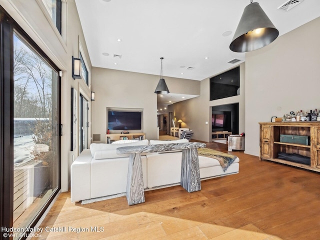 living area featuring light wood-style flooring, a towering ceiling, visible vents, and recessed lighting