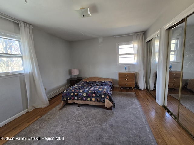 bedroom with multiple closets, a baseboard radiator, and wood-type flooring