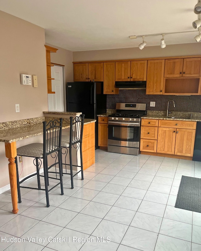 kitchen featuring sink, gas range, black fridge, dark stone countertops, and backsplash