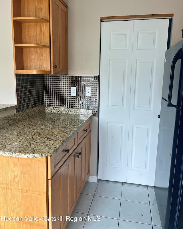 kitchen featuring black fridge, stone countertops, light tile patterned floors, and decorative backsplash