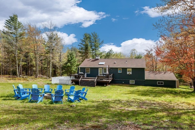 back of property with a deck, an outdoor fire pit, and a lawn