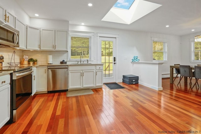 kitchen featuring a skylight, stainless steel appliances, sink, white cabinetry, and plenty of natural light