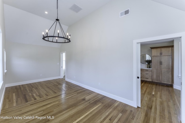 unfurnished dining area featuring high vaulted ceiling, wood-type flooring, and a notable chandelier