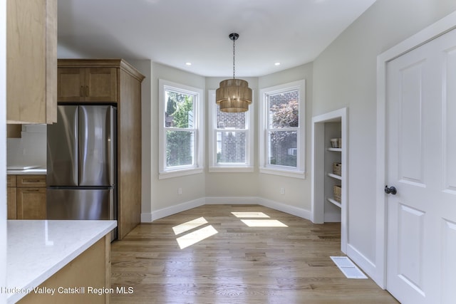 kitchen featuring hanging light fixtures, stainless steel fridge, light stone counters, and light hardwood / wood-style floors