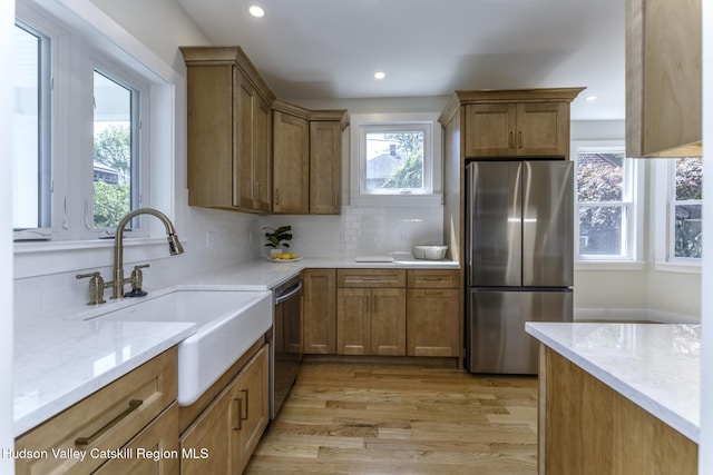 kitchen with light hardwood / wood-style floors, stainless steel appliances, backsplash, light stone countertops, and sink