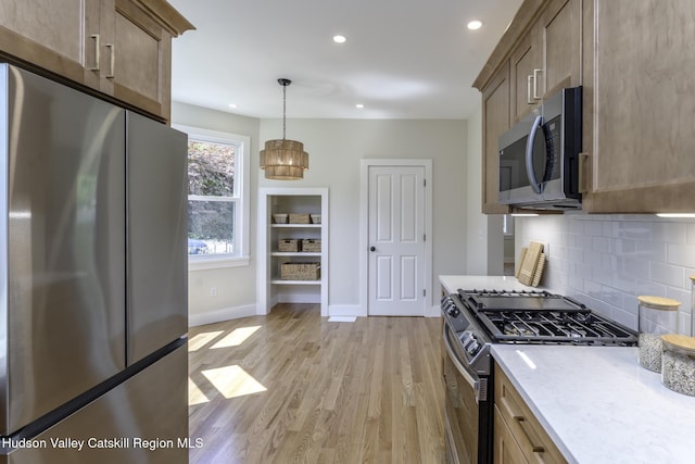 kitchen featuring pendant lighting, appliances with stainless steel finishes, decorative backsplash, light stone counters, and light hardwood / wood-style flooring