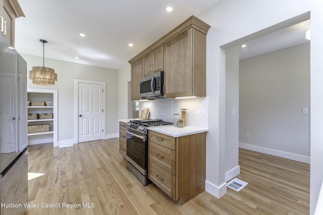 kitchen featuring stainless steel appliances, backsplash, hanging light fixtures, a notable chandelier, and light wood-type flooring