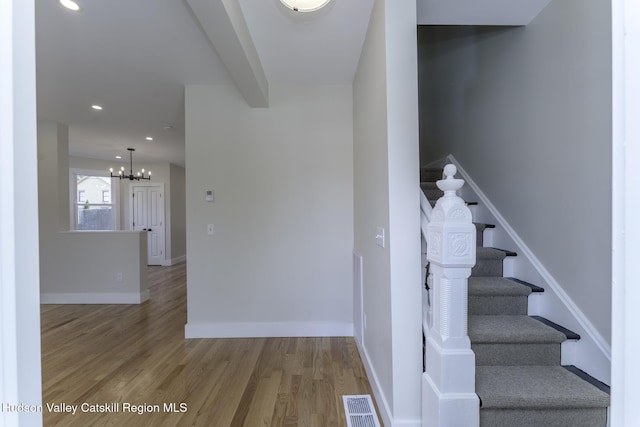 stairs with hardwood / wood-style floors, beamed ceiling, and a notable chandelier